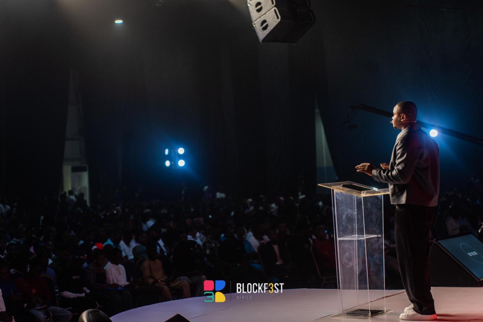 Idris at a clear lectern, speaking to a full hall at Blockfest Africa