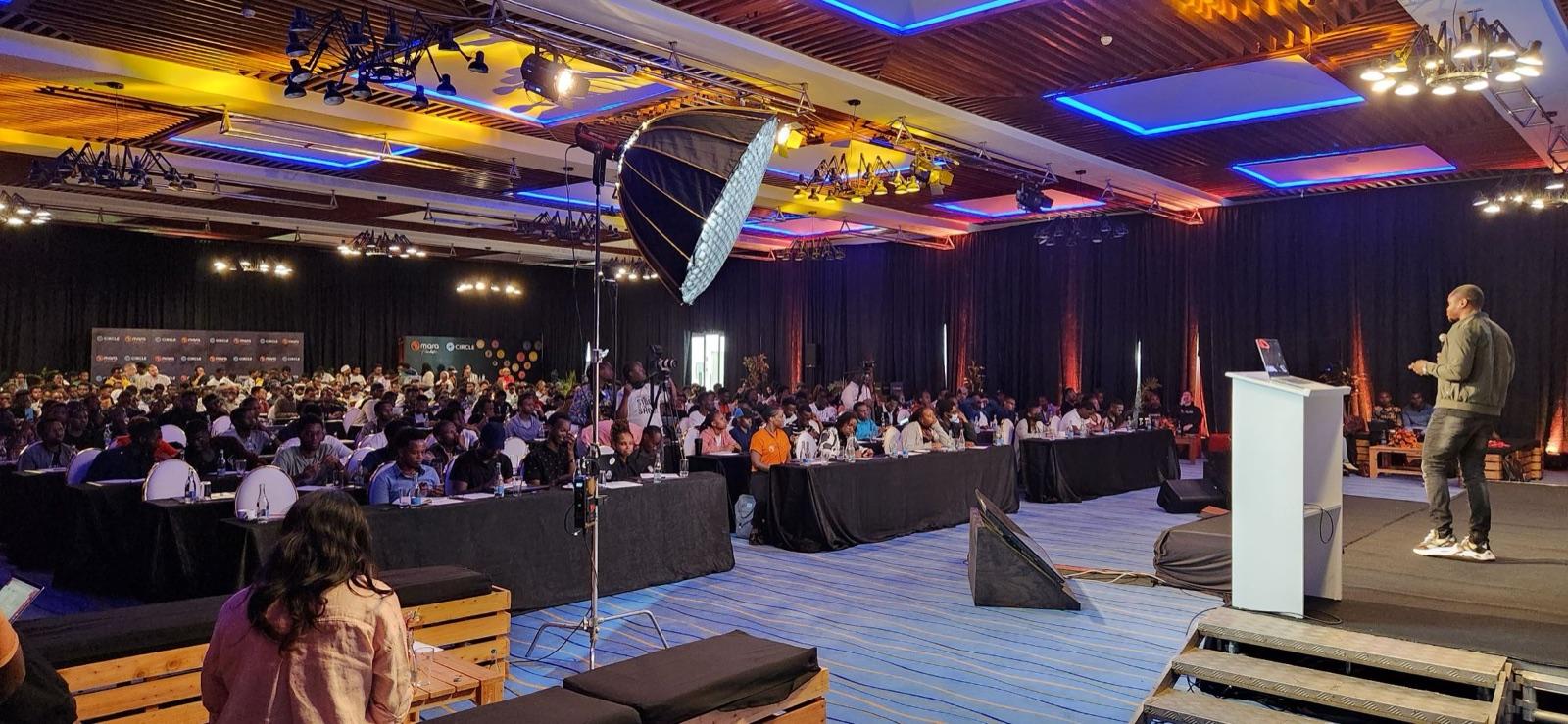 Idris presenting from the stage to rows of developers at long tables, with cameras and lights around the room